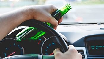 Young man driving a car with a bottle of beer